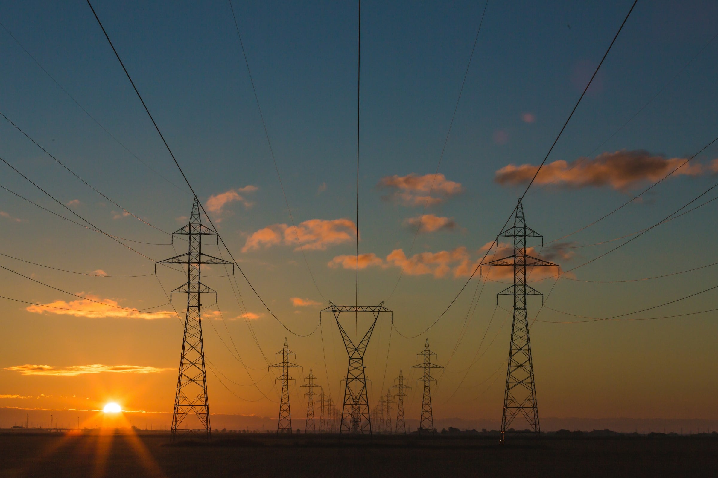 High-voltage transmission towers across open land at sunset